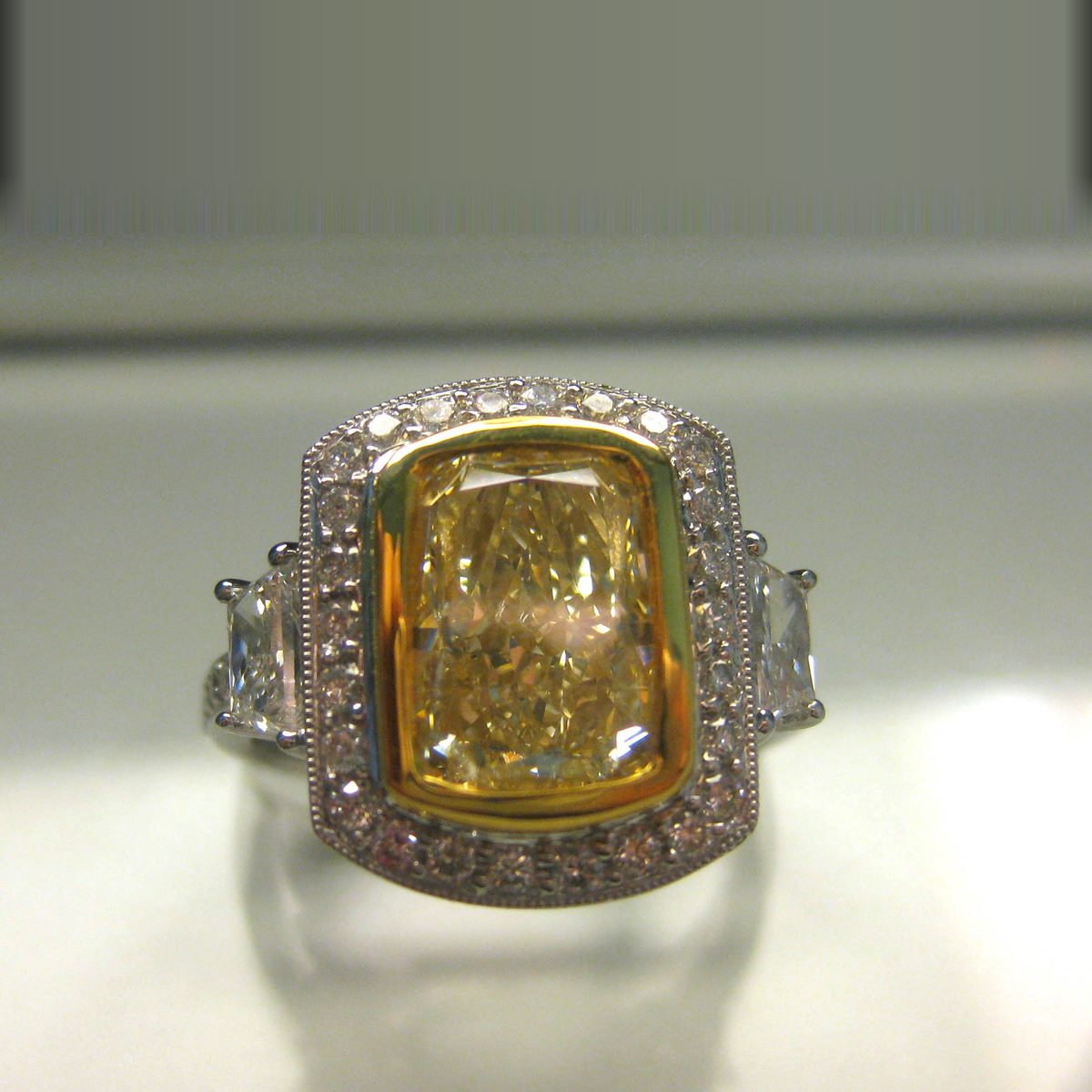 Fancy yellow cushion cut diamond three stone ring with a milgrain halo